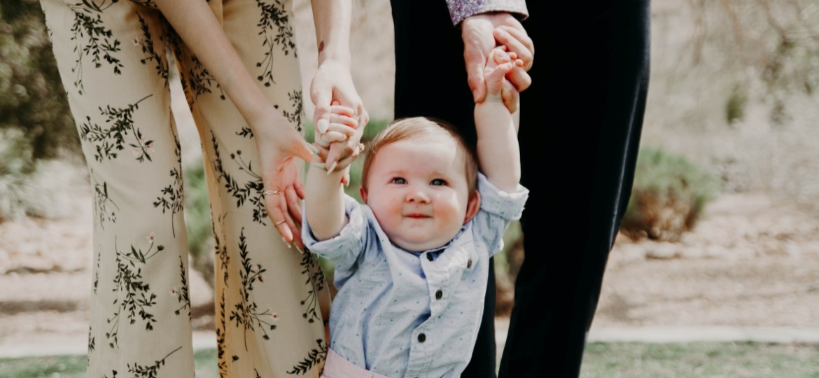 A baby holding the hands of parents