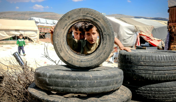refugee kids looking through the tyre. 