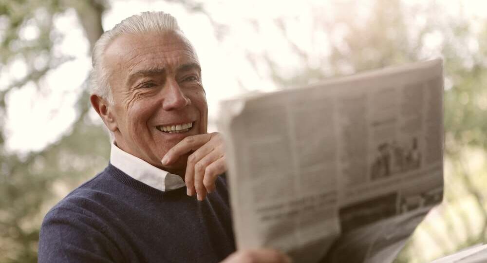 A senior citizen smiling while reading the newspaper