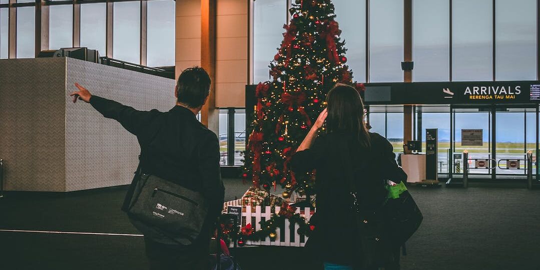 Two people standing in front of a Christmas tree at an airport