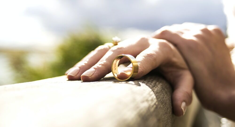 A person holding a wedding band with index finger