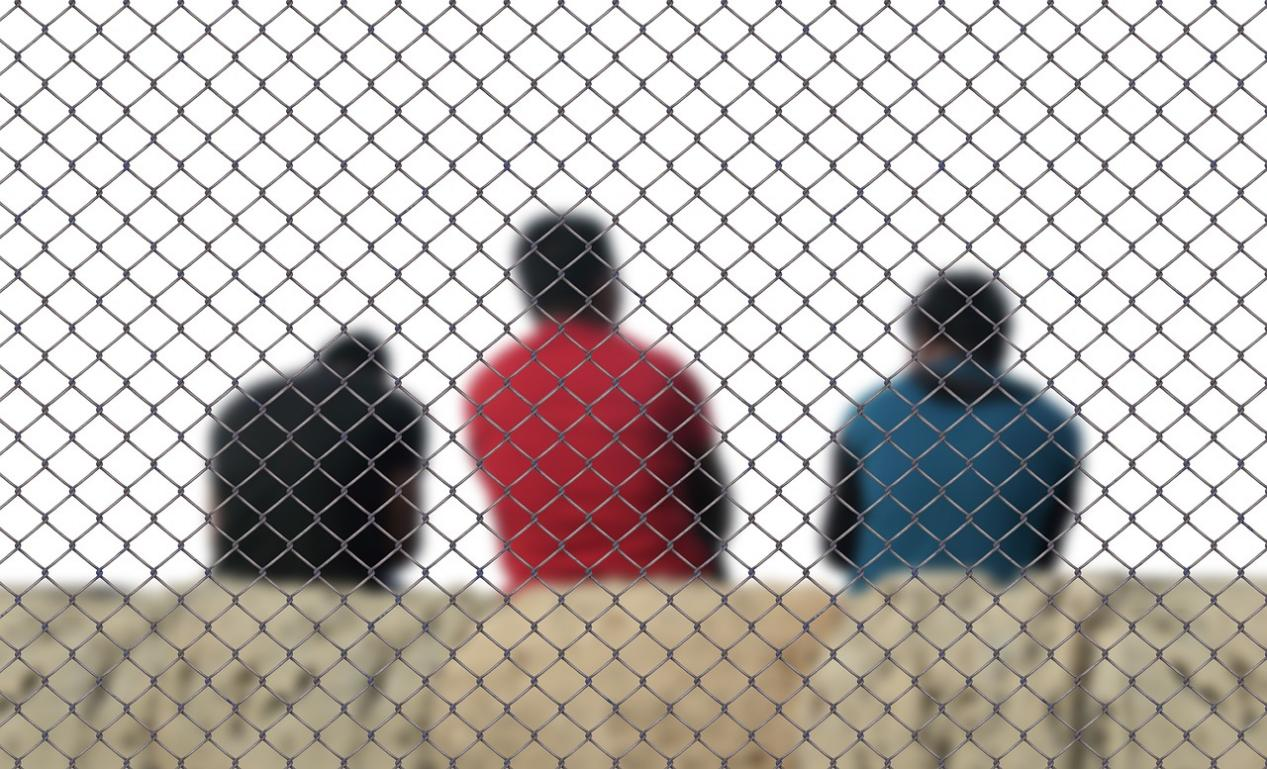 Three people behind a cage wall